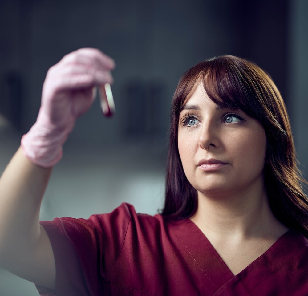 Eine Tierarzthelferin hebt ein gef&uuml;lltes Reagenzglas vor sich und betrachtet den Inhalt.