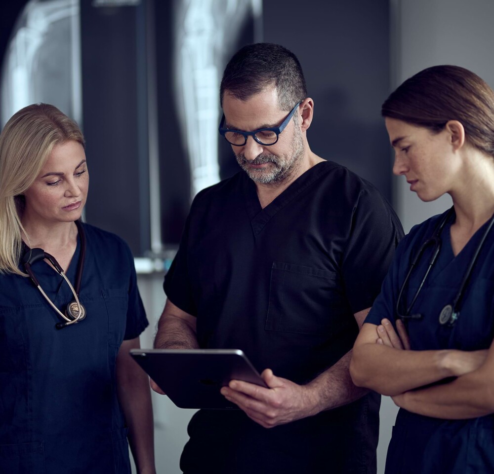 Herr Dr. Lautersack schaut mit zwei Tier&auml;rztinnen konzentriert auf ein Tablet. R&ouml;ntgenaufnahmen im Hintergrund.