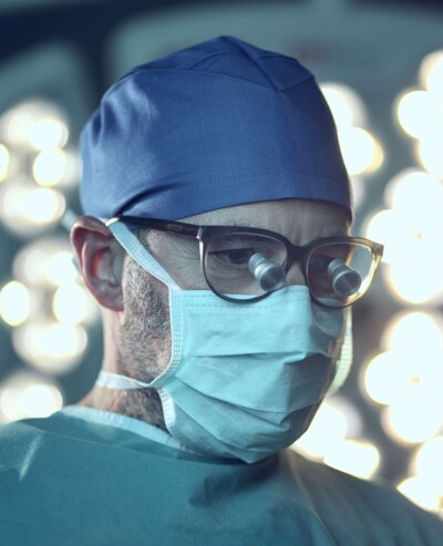 Nahaufnahme von Herr Dr. Lautersack mit blauer Arbeitsbekleidung, Mundschutz und Haube im OP-Saal.