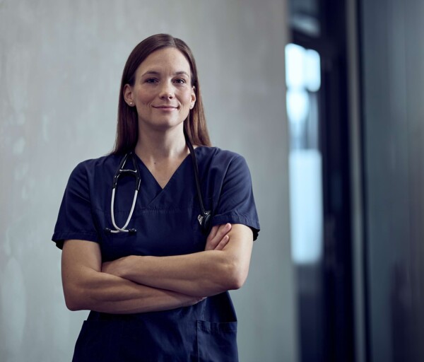 Frau Kl&uuml;ger steht selbstbewusst mit verschr&auml;nkten Armen im Gang.