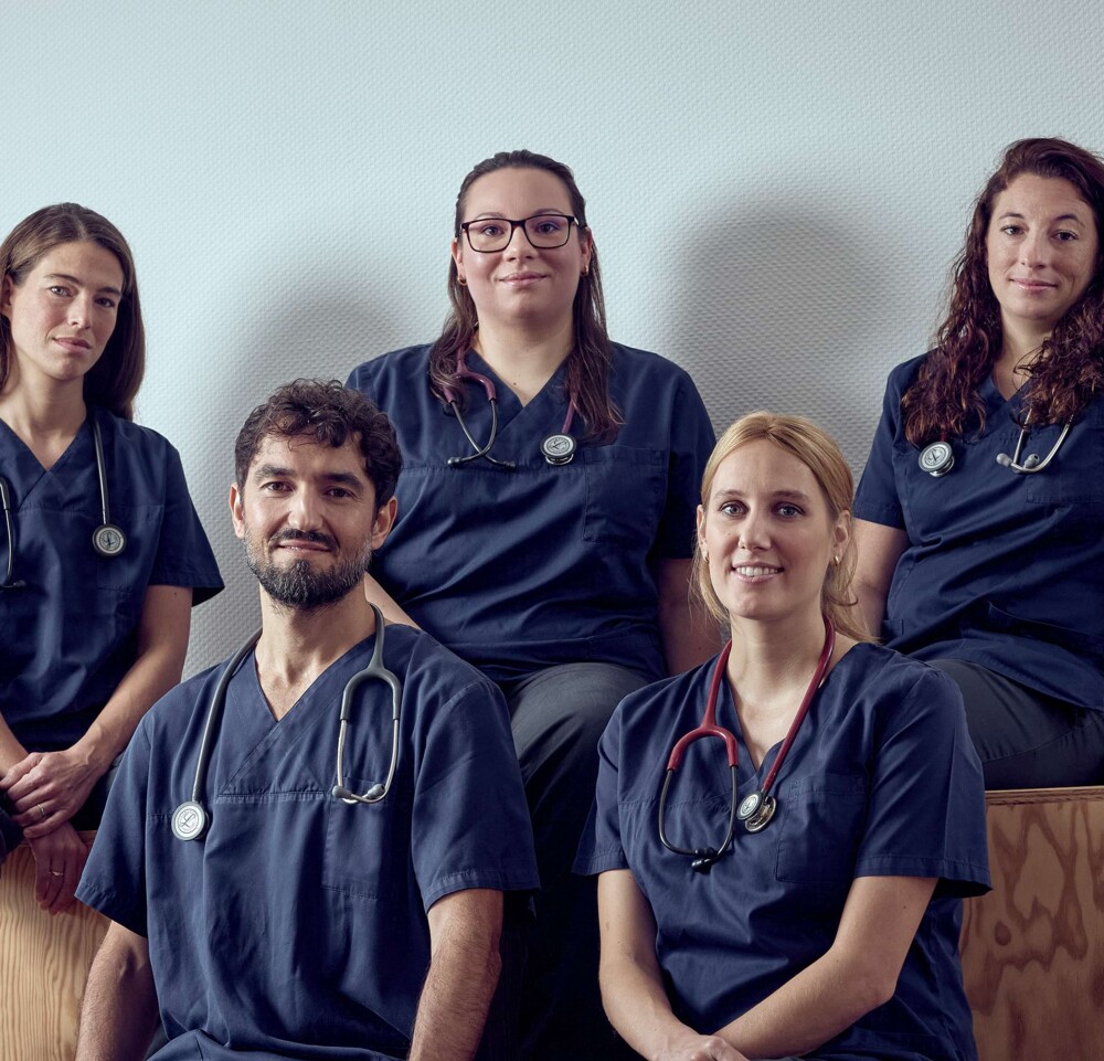 Ein f&uuml;nfk&ouml;pfiges Team sitzt auf h&ouml;lzernen Stufen und l&auml;chelt in die Kamera.