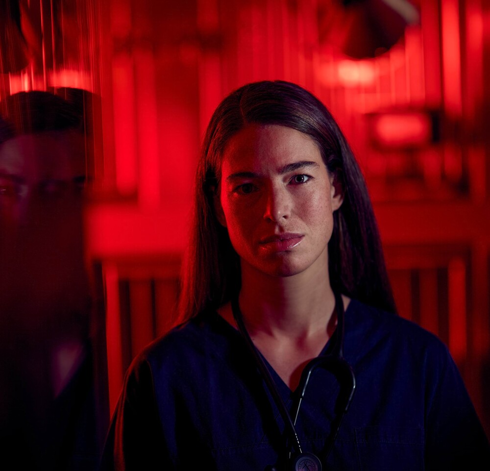 Eine Tier&auml;rztin sitzt in einem dramatisch rot beleuchteten Raum. In einer Scheibe ist ihre Reflektion zu erkennen.