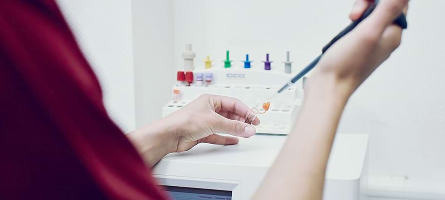 Nahaufnahme von H&auml;nden in einem Labor, die mit einer Pipette eine Fl&uuml;ssigkeit in ein kleines Probenr&ouml;hrchen f&uuml;llen.